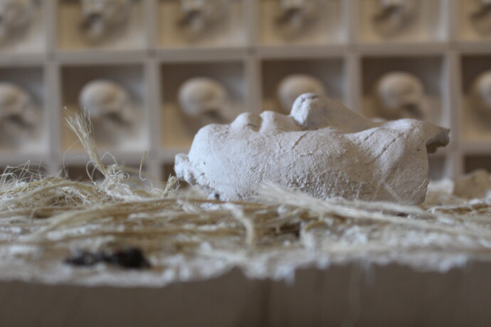 Death Without End. Raw plaster, ceramic, and ixtle. In the background: The Wall, a contemporary tzompantli of 100 plaster blocks. Perla Arroyo, 2026. Exhibition Mexican Skull: Identity and Memory, Museo de la Cancillería, Mexico City.